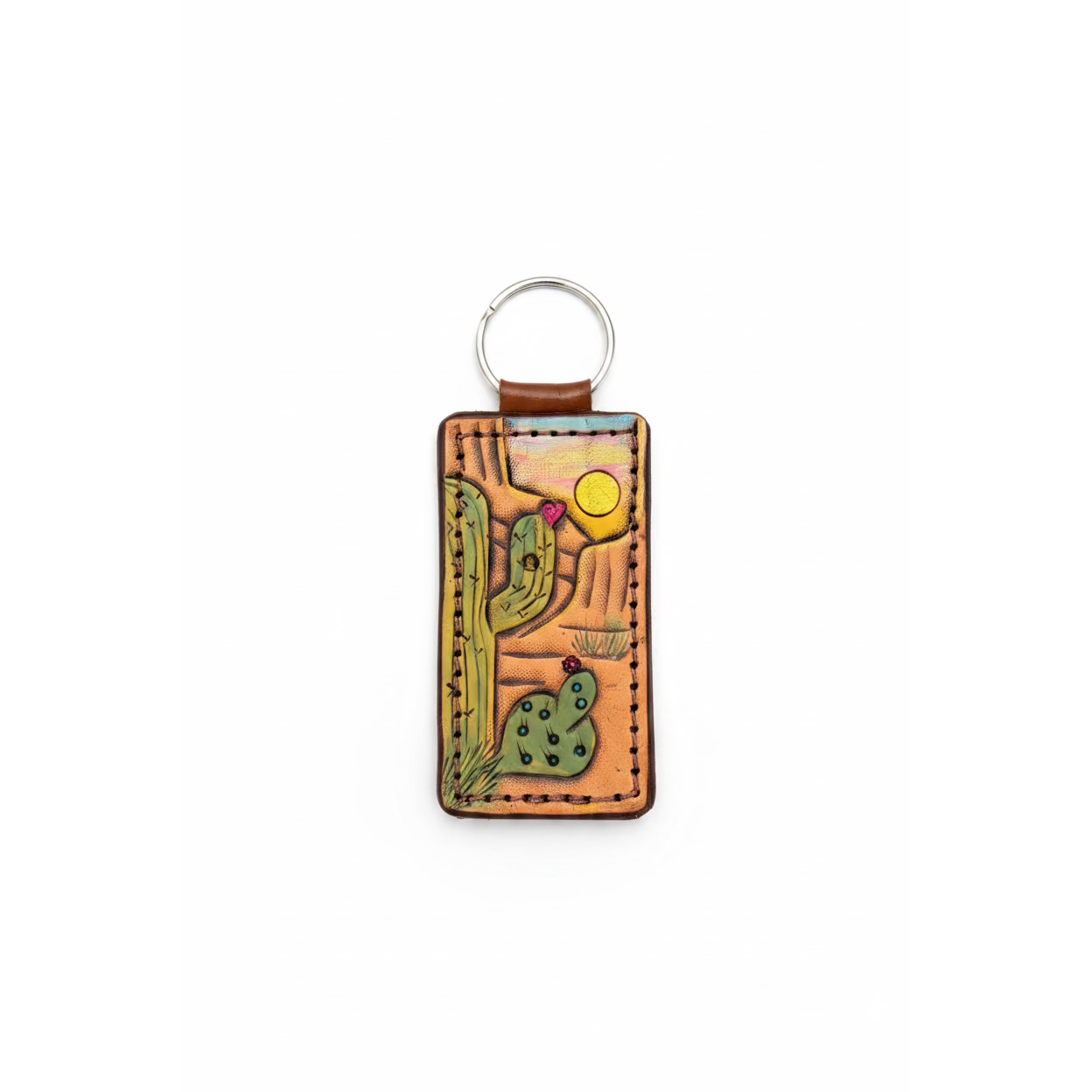 A rectangular hand-tooled leather keychain featuring a desert cactus design, resting on a rustic wooden surface.