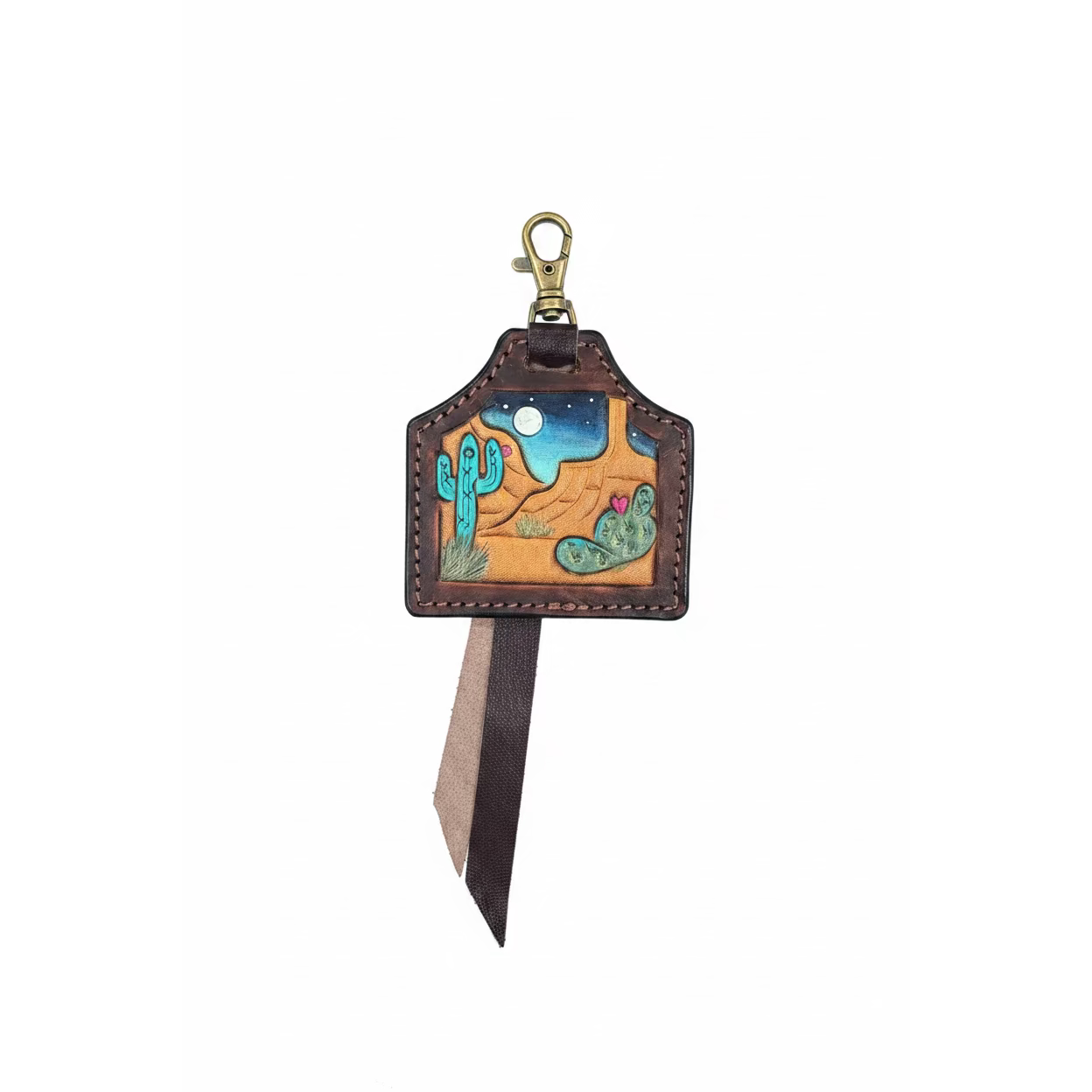 A handcrafted leather keychain or bag charm with a desert landscape design, featuring a brass clasp and a long leather ribbon tail, displayed on a dark gray background.