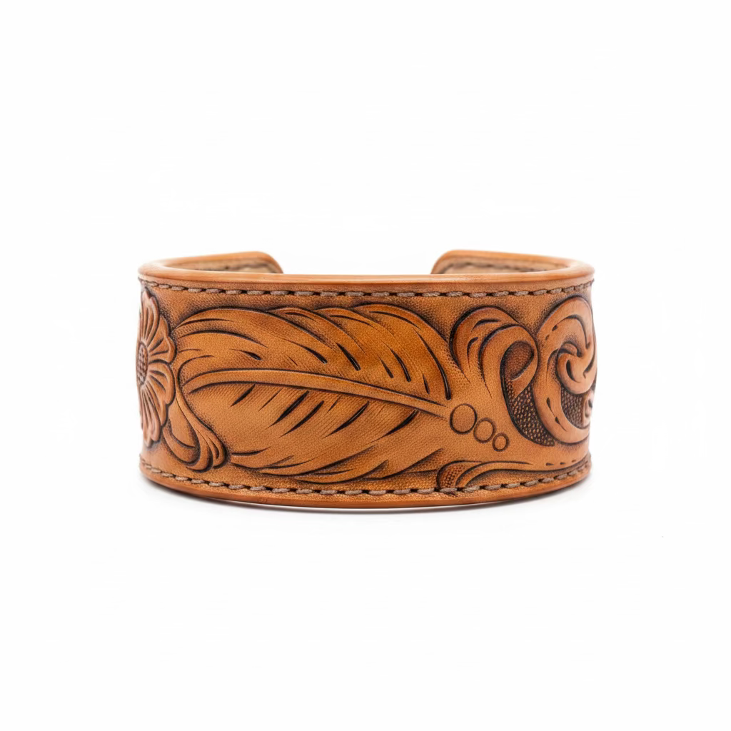 A wide tan leather cuff bracelet with hand-tooled floral and leaf patterns, displayed on a rustic wooden surface.