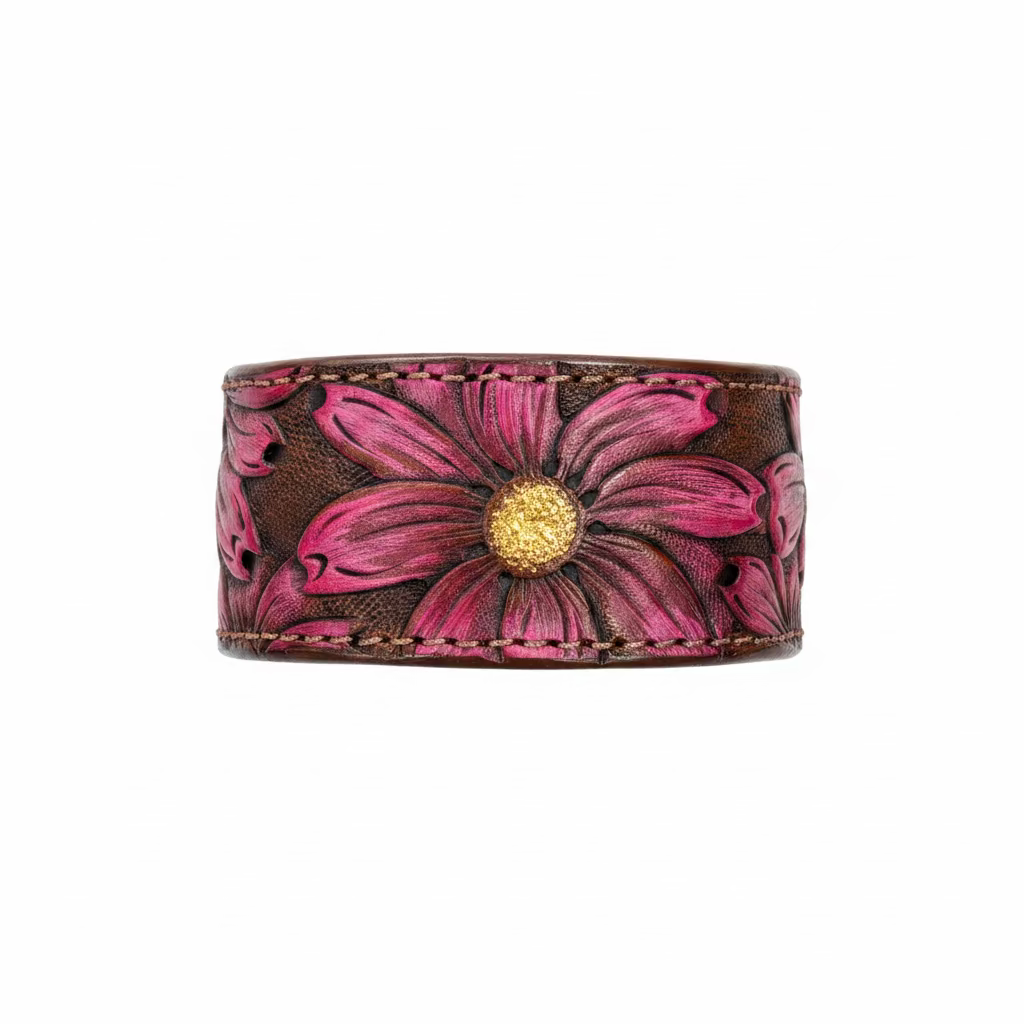 A hand-tooled leather cuff bracelet featuring a large pink and magenta daisy flower with a gold center, displayed on a rustic wooden surface.