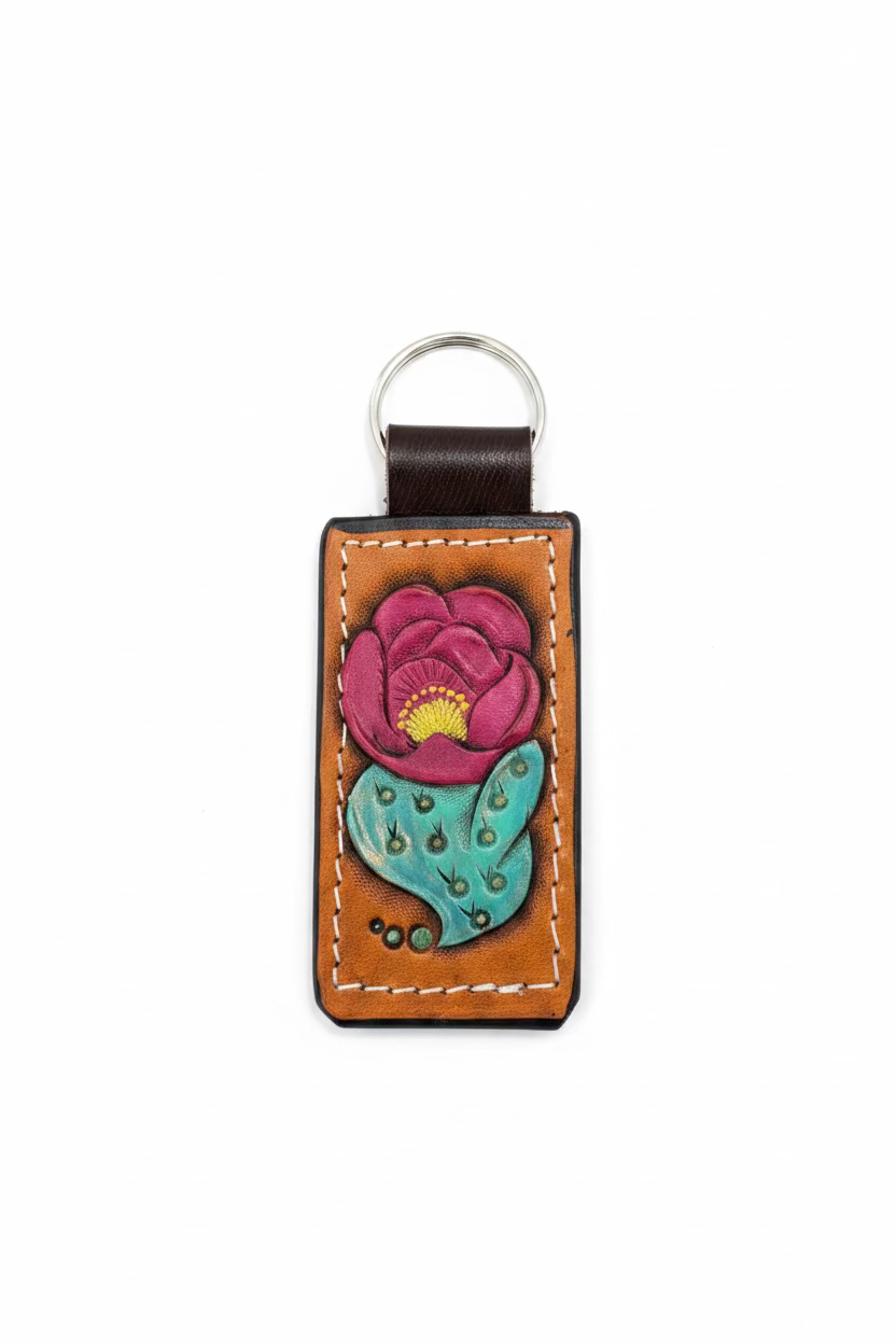 A handcrafted brown leather keychain featuring a hand-painted lotus flower with pink petals, a yellow center, and a teal-green stamen, resting on a rustic wooden surface.