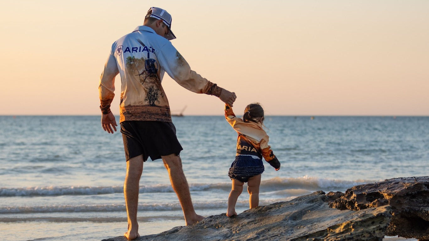 Man and child standing on rocks at the beach during sunset