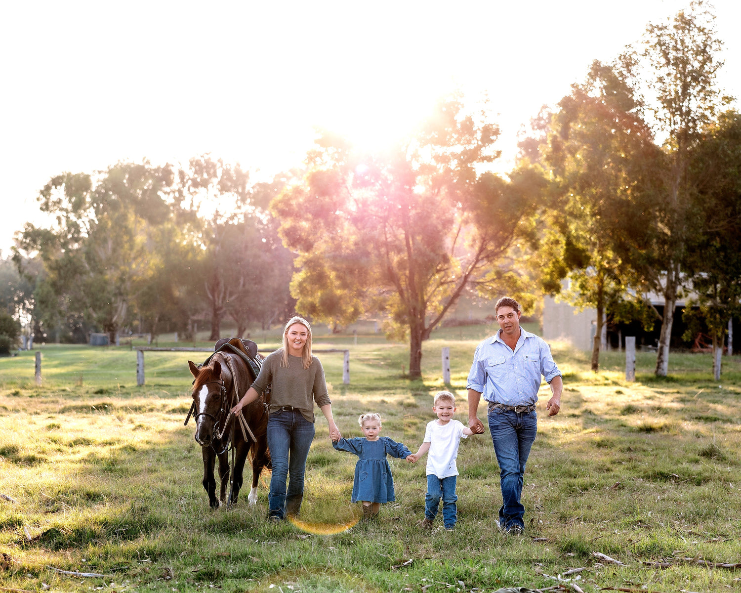 Family of four with a horse walking in a grassy field with trees and a fence in the background.
